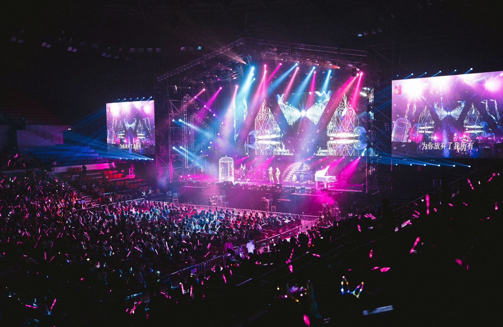 Arena concert with pink and blue stage lighting over a full crowd