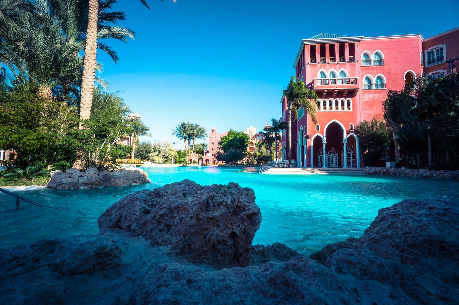 A resort swimming pool in front of a pink hotel building